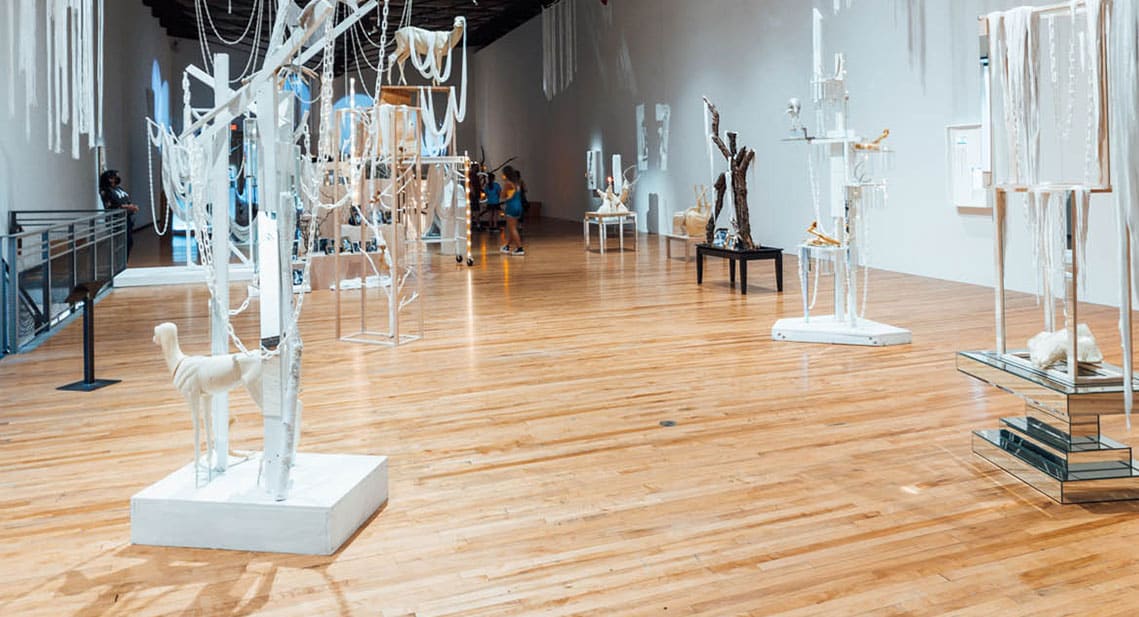 Art gallery interior featuring various abstract sculptures displayed on pedestals and suspended installations, with visitors observing the artwork near North Adams hotels.