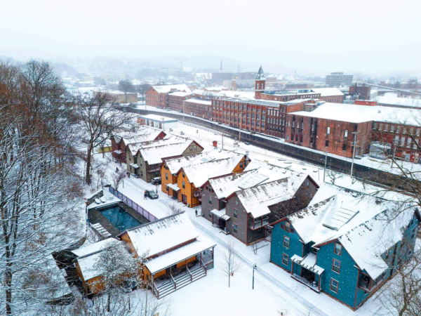 Aerial view of a snow-covered industrial town with red brick buildings near North Adams, Massachusetts, and a dusting on trees and roads.