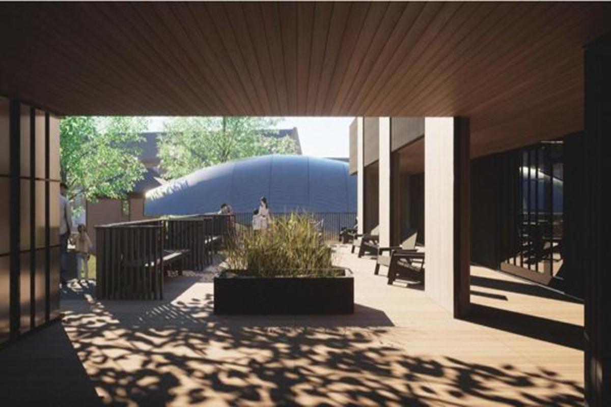 Wooden terrace with benches, planters, and sunlight casting shadows; people are standing and walking in the outdoor space.